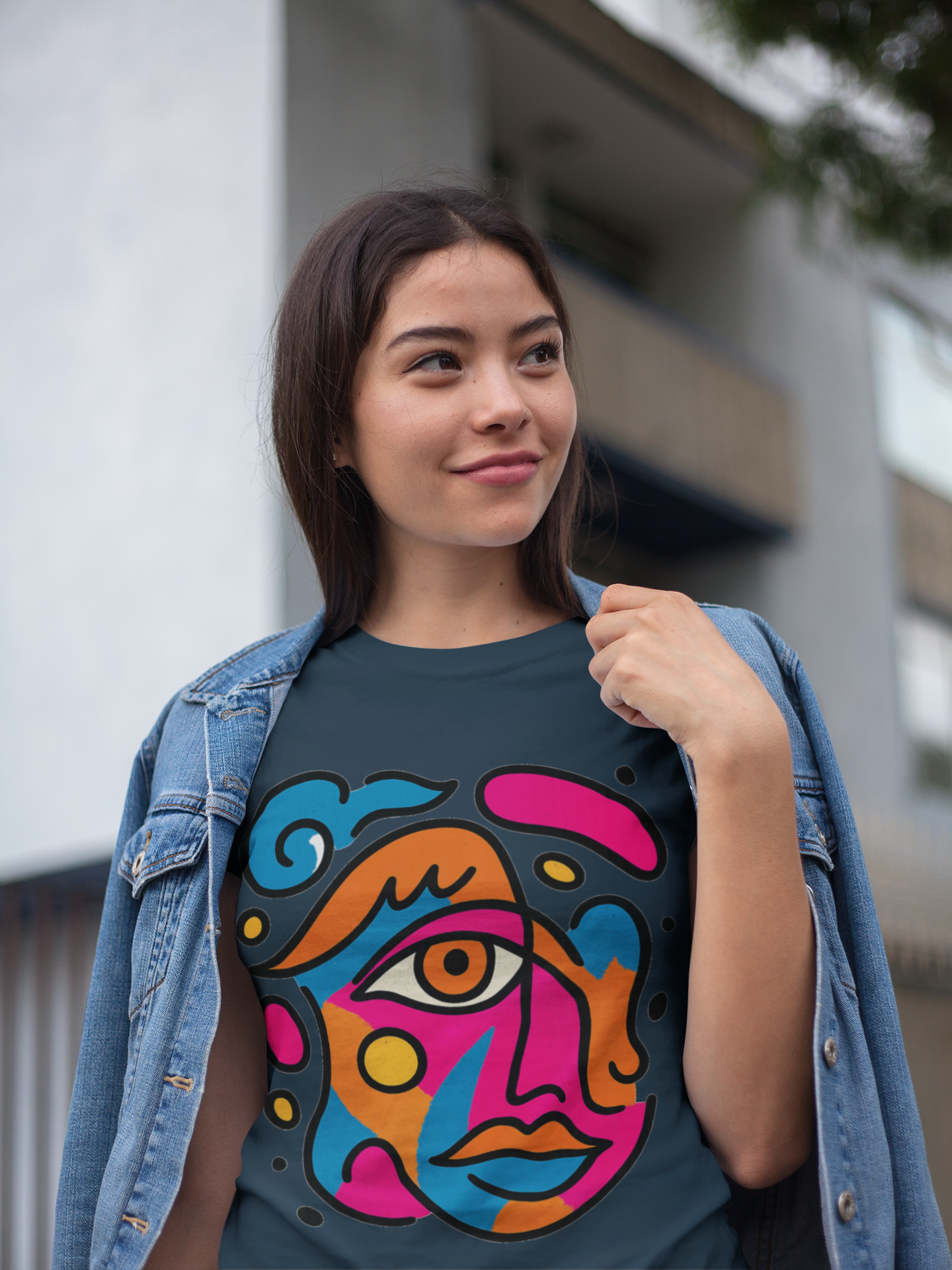 Woman wearing dark teal t-shirt with vibrant abstract pop art face print in pink, blue, orange and yellow colors and denim jacket
