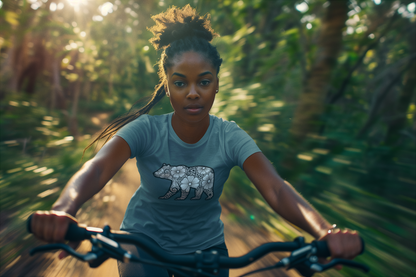 Woman riding bicycle in forest wearing teal t-shirt with geometric bear print

