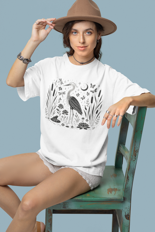 Woman sitting on chair wearing white t-shirt with heron and water plants print
